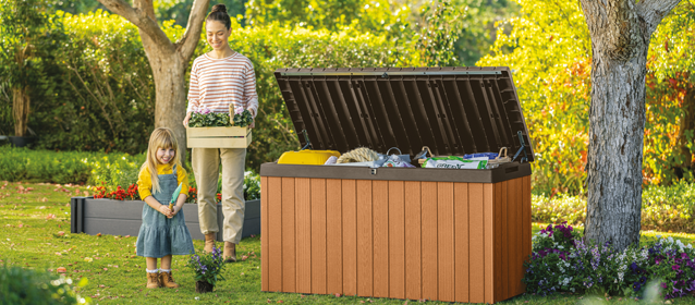A women adding garden items to a Darwin storage box whist another women is carrying a wooden crate with flowers