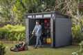 A man outside his open shed working on his lawnmower