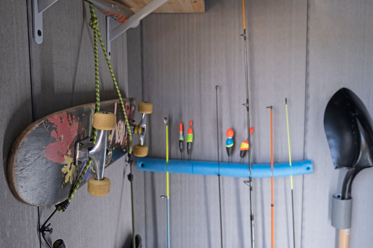Various storage options inside a shed using bungees and foam rolls to hand up a skateboard and keep fishing rods standing up in place