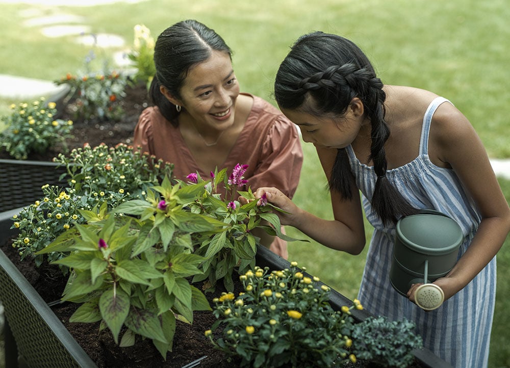 mother and daughter inspect the plants growing in their garden bed