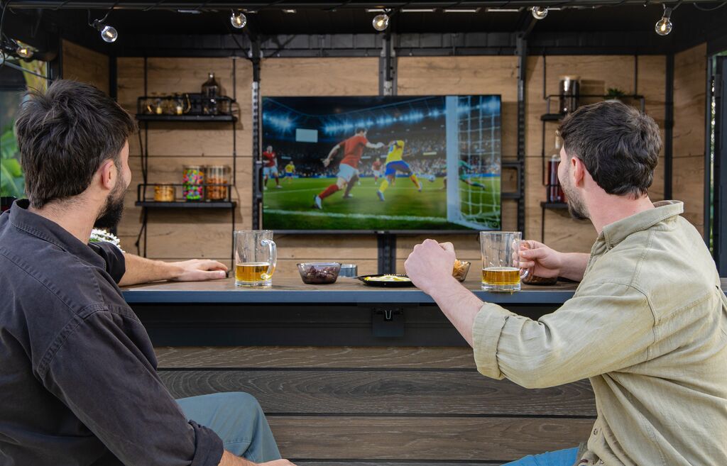 2 friends watching a soccer game in an outdoor bar shed