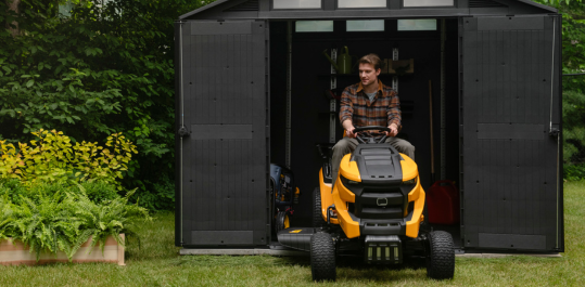man driving a riding lawnmower from a shed