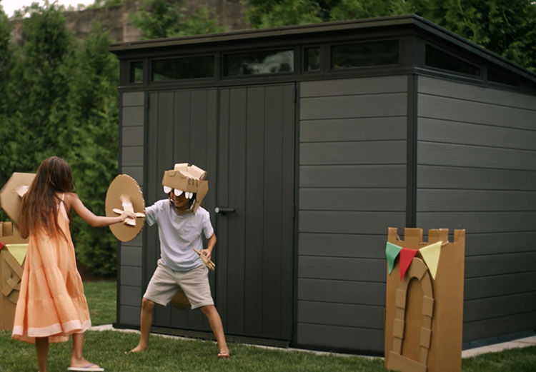 2 kids playing dress up in front of a storage shed