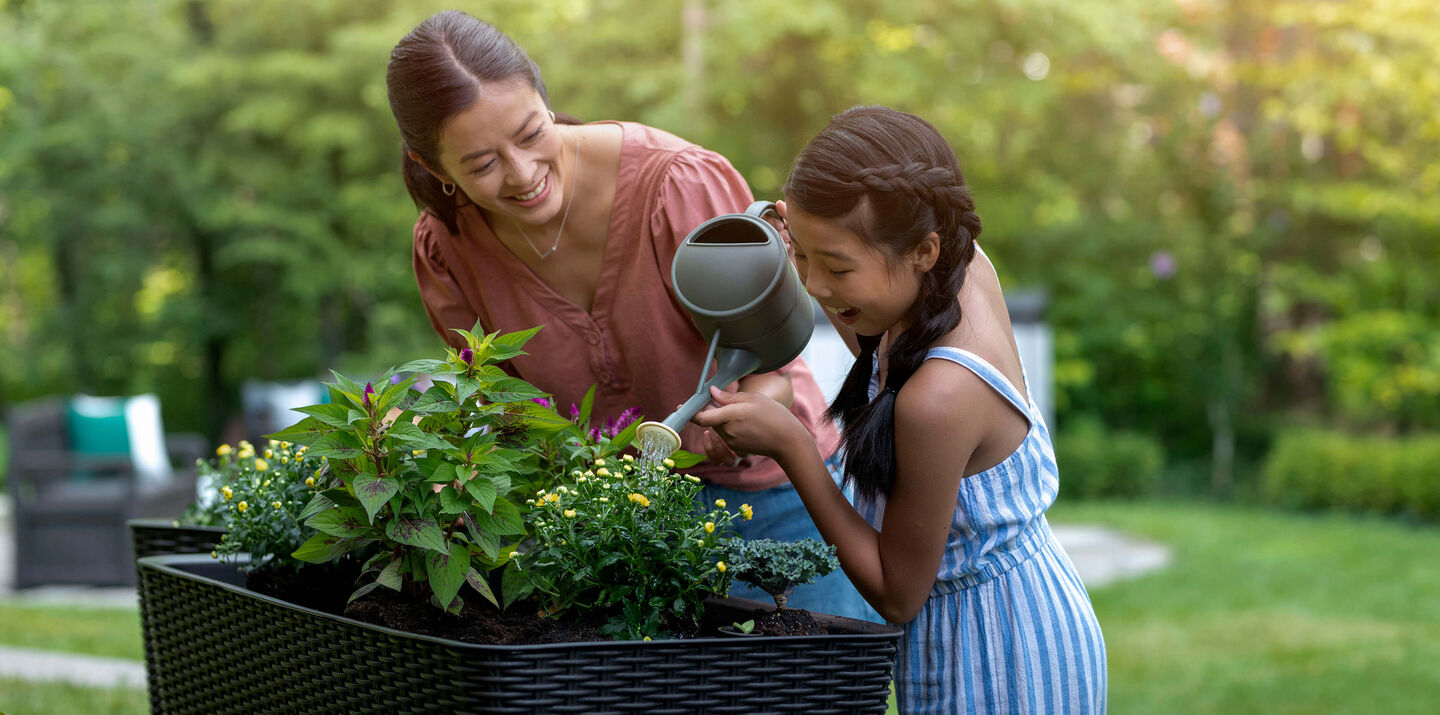 Mother and daughter water their plants growing in their elevated garden bed from Keter