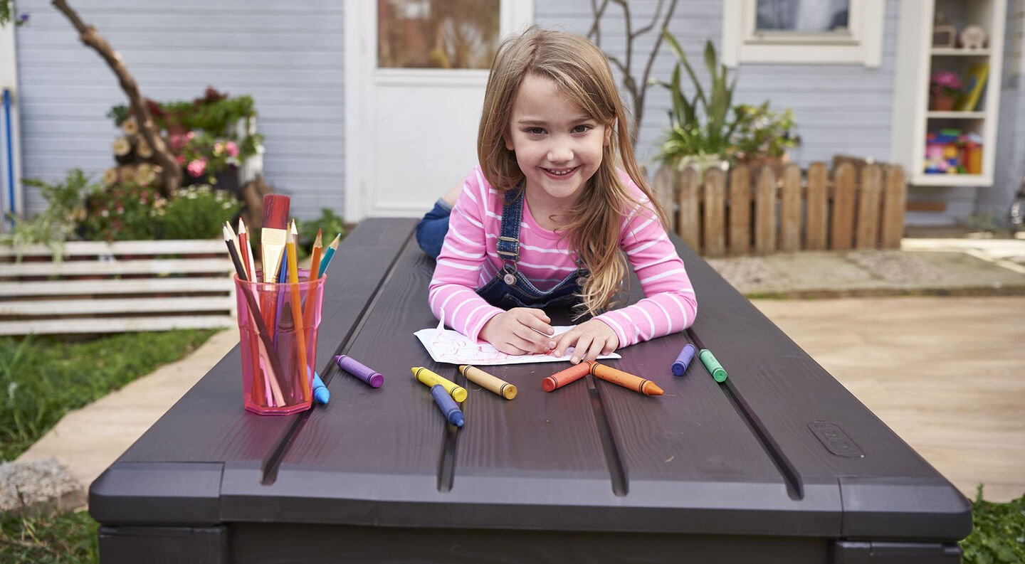 Little girl coloring on a deck box