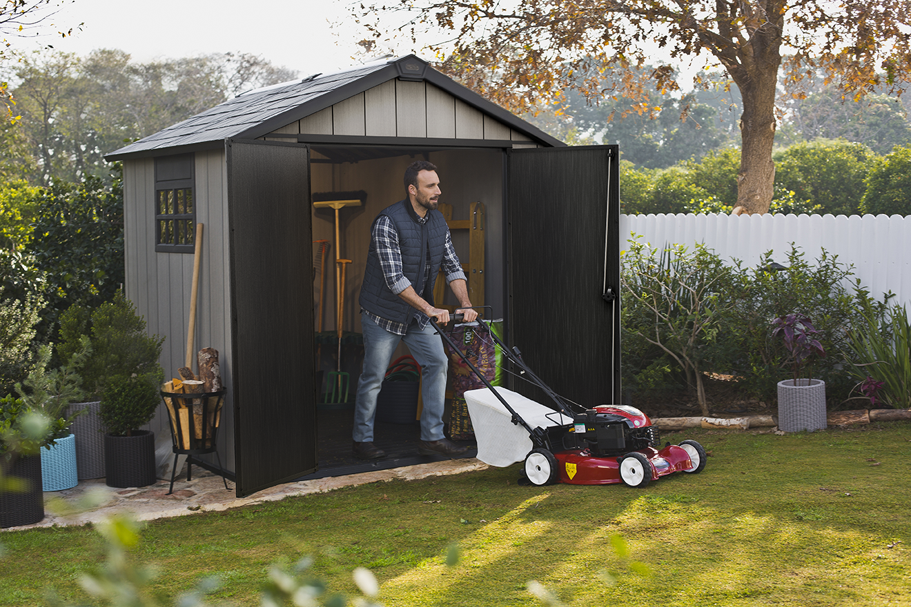 Man taking his lawn mover out of his backyard storage shed