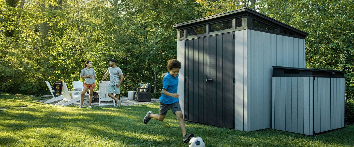 Little boy playing soccer in front of a shed