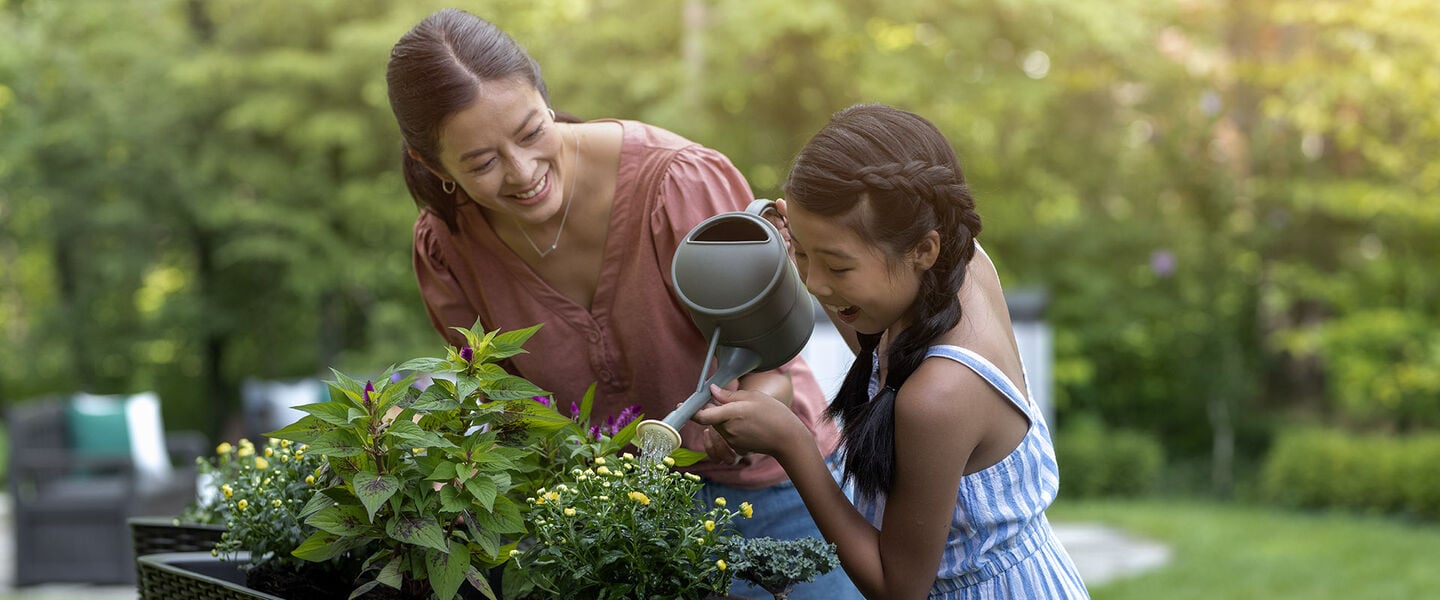 Mother and daughter watering plants in a raised garden bed