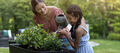 Woman and child watering plants in backyard in grey Keter planter.
