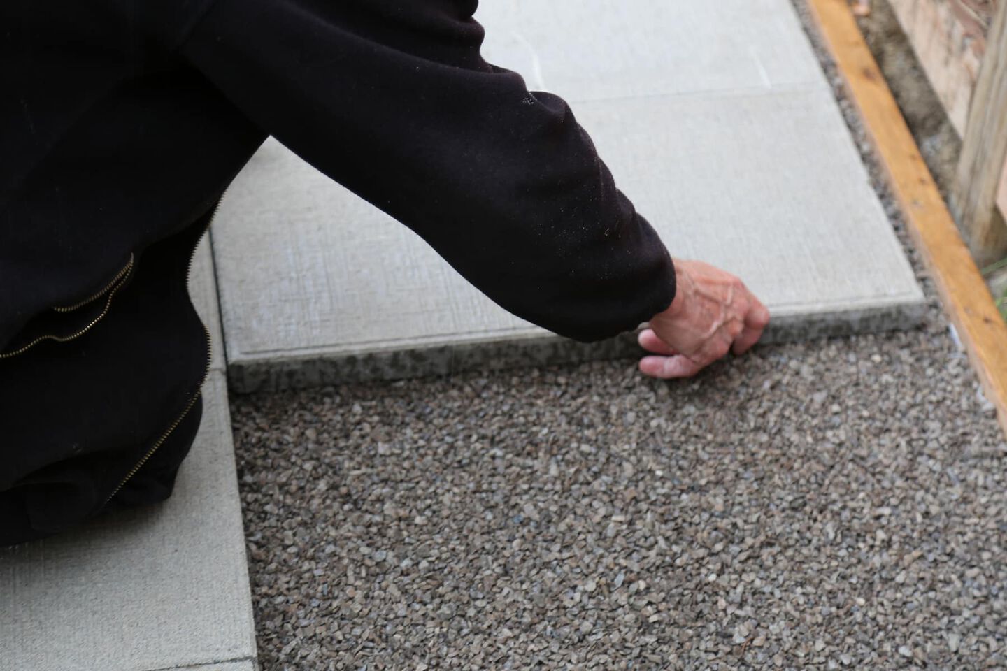 man placing a concrete tile over a gravel base