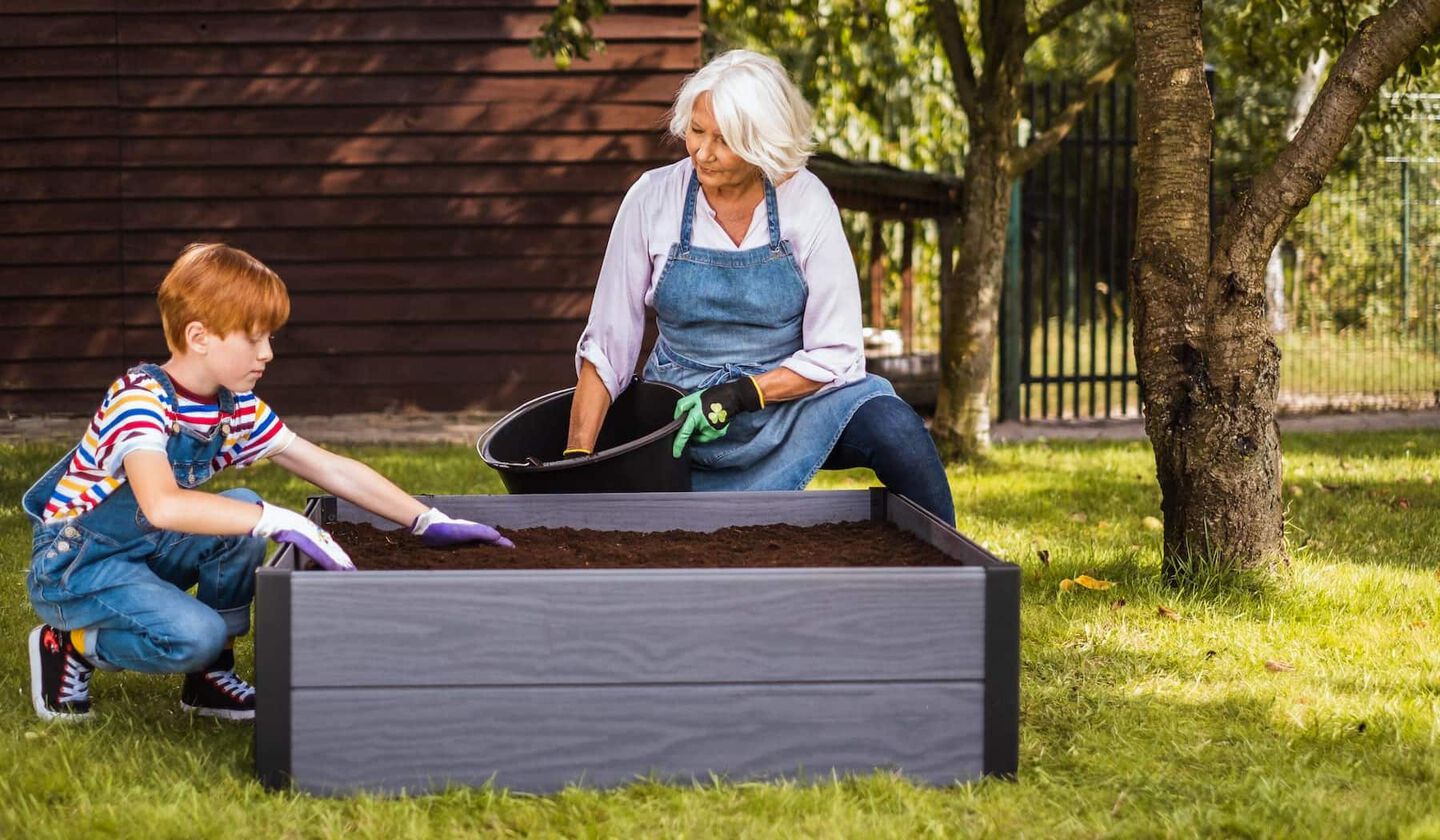 grandma with kid adding soil to a garden bet