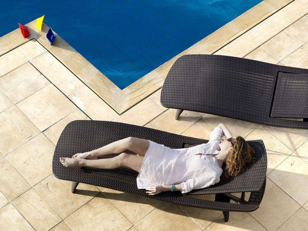 Woman on a sun lounger next to her backyard pool