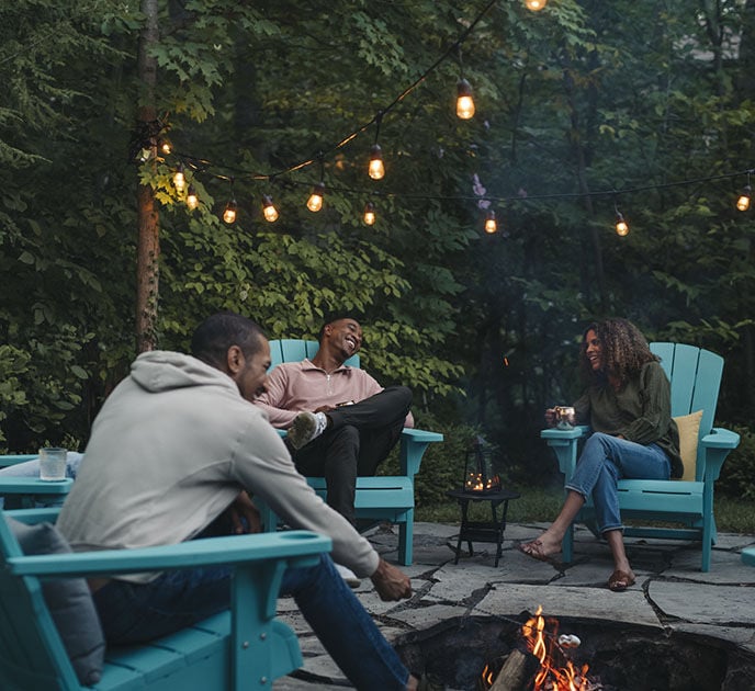 three friends around a bonfire toasting marshmallows while sitting in Keter Alpine Adirondacks