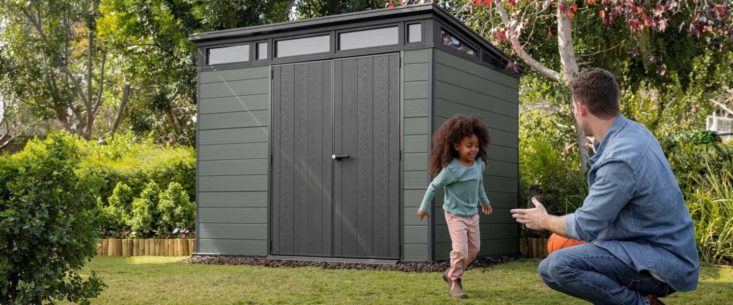 Father and daughter playing in the backyard next to storage shed. 