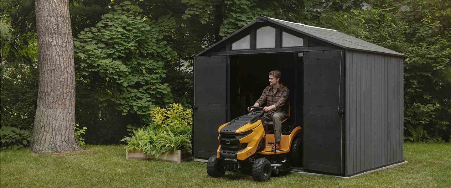 Man on riding lawn mower in large gray keter Stronghold shed
