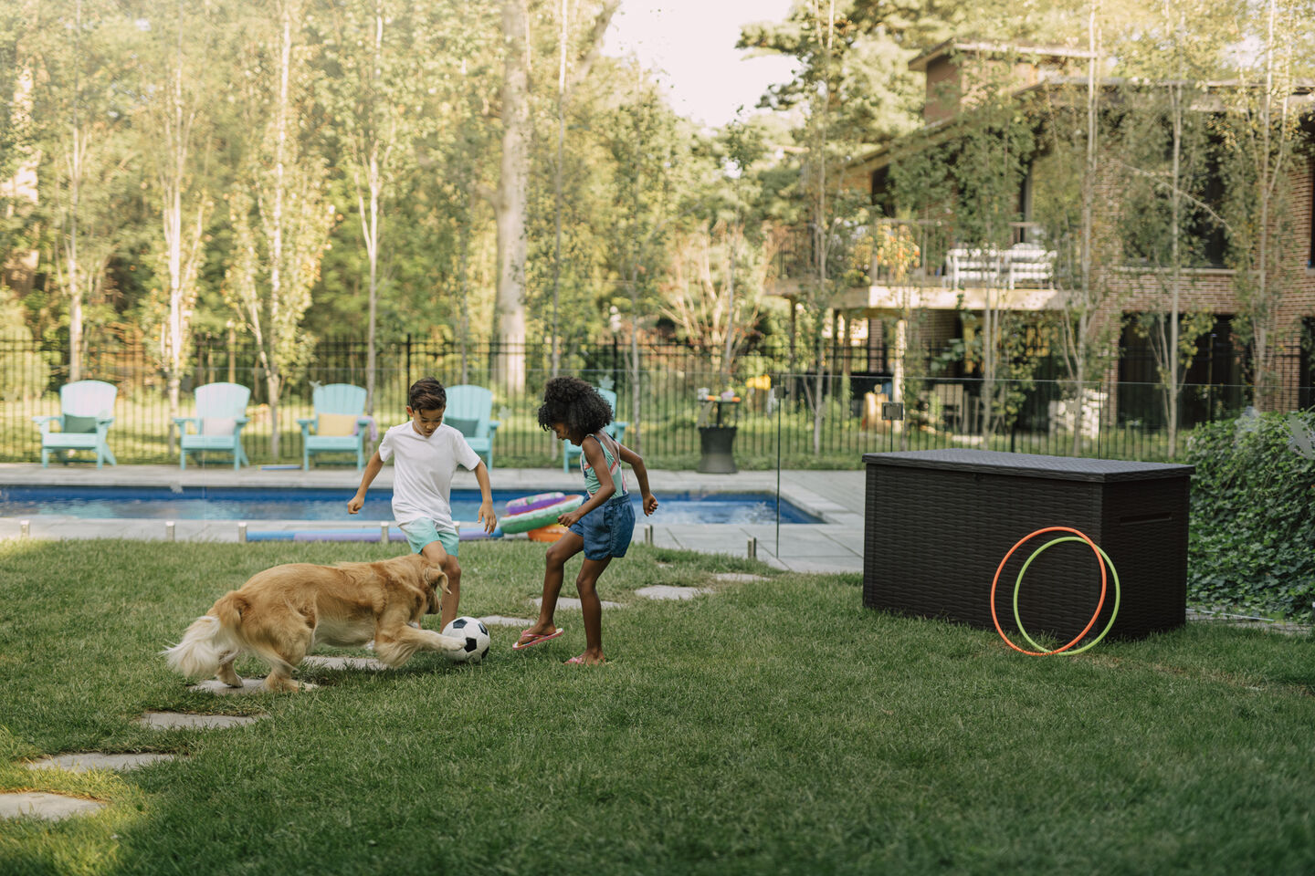 Kids playing soccer with their dog by the pool