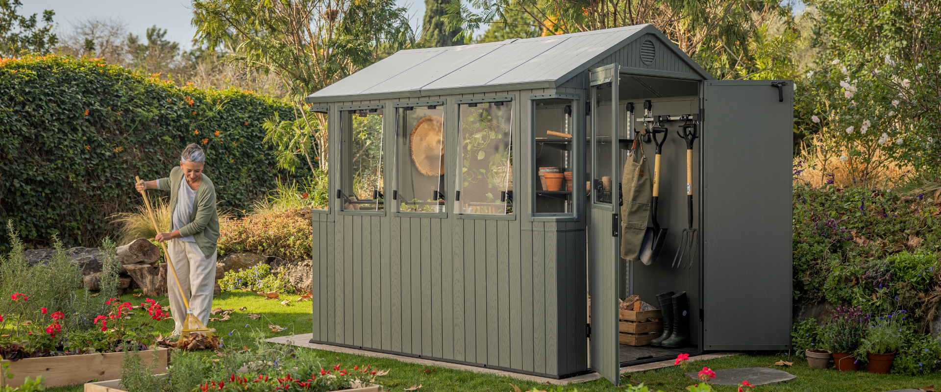 Femme ratissant les feuilles à côté d'une serre de jardin verte