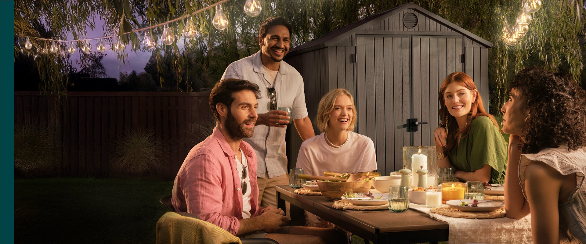 A group of friends around the Signature Porto table in front of the Darwin 6x8 grey shed 