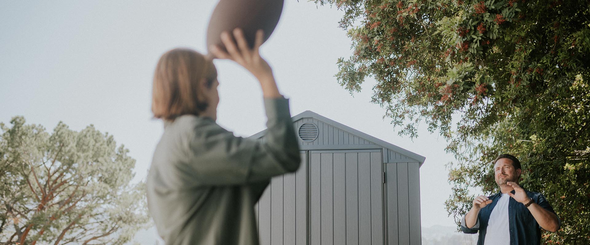 Boy throwing football in front of Keter gray Darwin shed